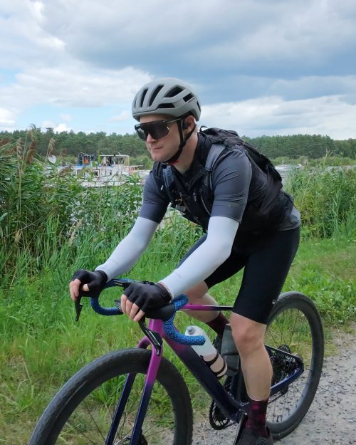 Tobias on his gravel bike on a gravel path by a lake, helmet and sunglasses on
